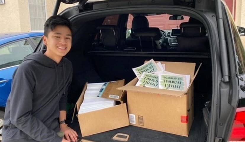 Andrew Diep-Tran standing next to boxes of financial literacy books that he plans to donate on behalf of his non-profit.